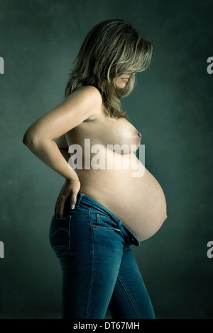 Belle femme enceinte en jeans posant devant un fond sombre Banque D'Images