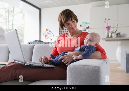 Mère et bébé garçon couchée sur un canapé avec un ordinateur portable Banque D'Images