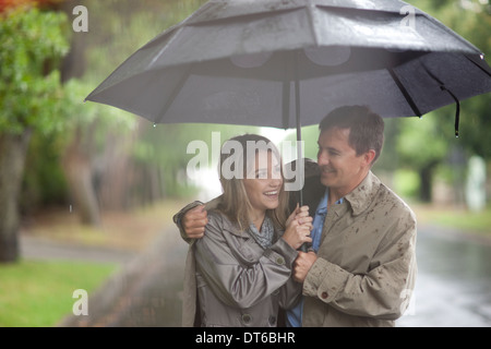 Jeune femme et mature man walking in rainy park Banque D'Images