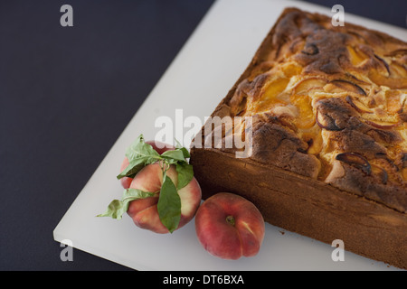 Un gâteau aux pêches au four carrés sur une carte dotée de pêches fraîches. Les fruits. Aliments biologiques frais dans une ferme avec une herbe en garniture. Banque D'Images