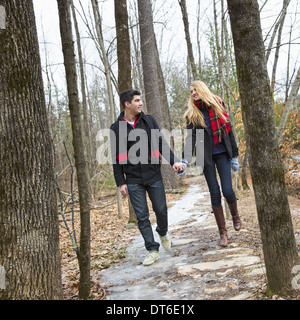 Un couple marche main dans la main à travers un bois en hiver.