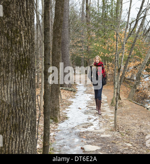 Une femme dans un manteau d'hiver et foulard rouge marchant dans un chemin de bois, en hiver. Banque D'Images