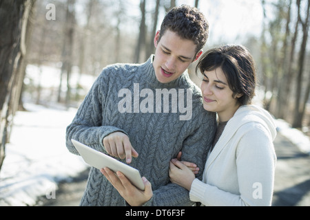 Un couple à la recherche à un ordinateur tablette. Debout sur une journée d'hiver dans les bois. Banque D'Images