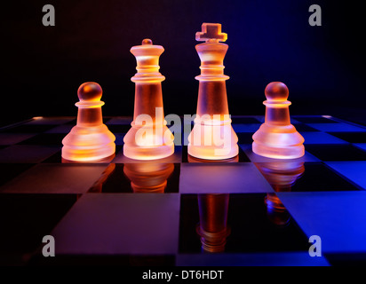 D'échecs en verre sur un échiquier éclairé par une lumière colorée en bleu et orange et placés sur un échiquier en verre Banque D'Images
