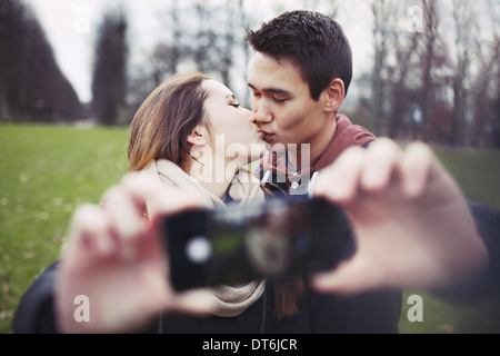 Lovely young couple taking self portrait tout en embrassant au parc. Teenage boy and girl with smartphone à l'extérieur. Banque D'Images