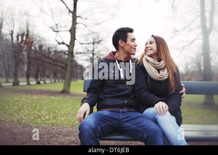 Couple assis sur un banc à l'extérieur pendant la saison d'hiver. Asian teenage couple dans des vêtements chauds assis sur banc de parc. Banque D'Images