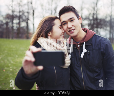 Young couple taking pictures en utilisant un téléphone intelligent au parc. Teenage boy and girl in love photographier eux-mêmes Banque D'Images