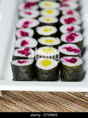 Photo verticale de rouleau de sushi mariné sur plaque blanche avec tapis bambou naturel en dessous Banque D'Images