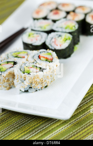 Libre photo verticale de rouleaux de sushi à la main, le remplissage plaque blanche, et baguettes en arrière-plan avec la texture green Banque D'Images