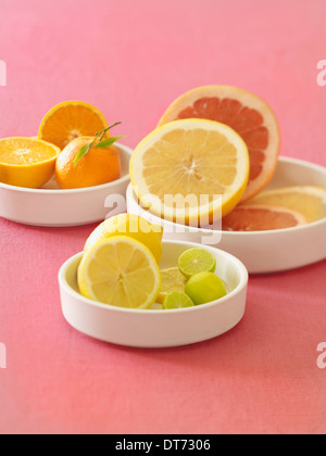 Un plateau blanc avec des oranges, orange sanguine, pamplemousse, citron et citron vert sur un fond de tissu rose. Banque D'Images