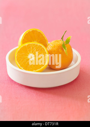 Un bol blanc avec des oranges ensemble et couper sur un fond de tissu rose. Banque D'Images