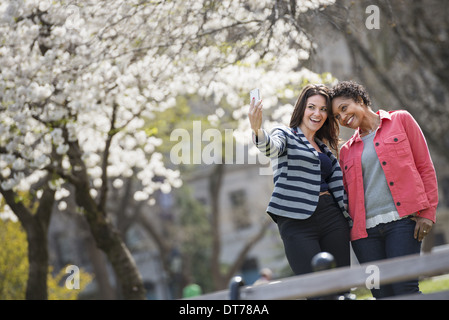 Temps de printemps. New York City park. Une jeune femme tenant un téléphone pour prendre une photo d'elle-même et d'un compagnon. Banque D'Images