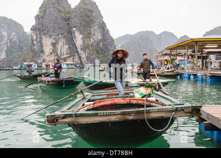 Une femme en chapeau conique et de l'ouest lignes robe un bateau en bambou pour les touristes dans un village de pêcheurs flottant. Banque D'Images