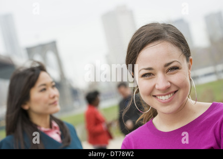 Passage sur le pont de Brooklyn, l'East River. Quatre amis dans le parc de la rivière, l'un souriant à la caméra. Banque D'Images