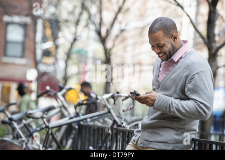 Un homme à l'aide de son téléphone. Un groupe de personnes dans l'arrière-plan. Rack à vélo. Banque D'Images