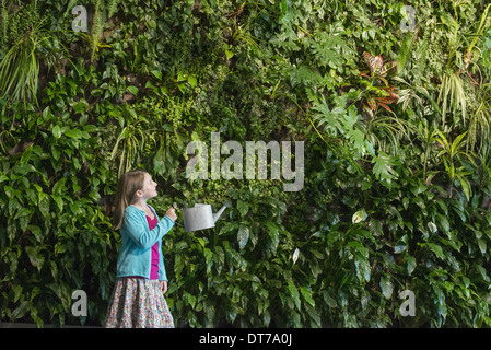 Une jeune fille debout devant un mur recouvert de fougères et plantes grimpantes. Banque D'Images