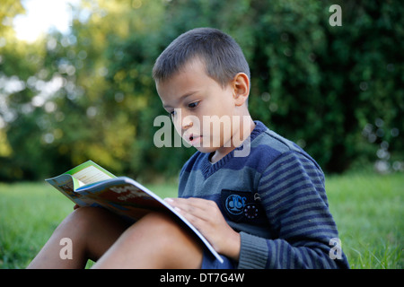 Garçon de 7 ans la lecture d'un livre chrétien dans un jardin Banque D'Images