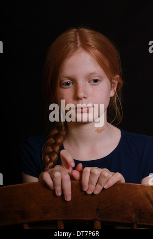 Un bel enfant à tête rouge avec ses cheveux dans une tresse fixe de l'appareil photo. Elle a l'air pensive l'arrière-plan est sombre. Banque D'Images