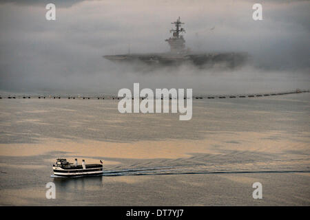 San Diego, CA, USA . Feb 11, 2014. Un laissez-passer de traversier de banlieue l'US Navy porte-avions nucléaire USS Ronald Reagan enveloppé dans le brouillard alors qu'elle s'assoit à son poste à quai, le 11 février 2014 à San Diego, CA. Credit : Planetpix/Alamy Live News Banque D'Images