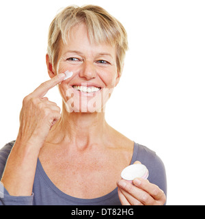 Smiling elderly woman putting Lotion soins de la peau sur son visage Banque D'Images