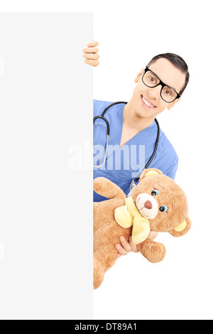 Young male nurse holding a teddy bear et jeter derrière panneau vierge Banque D'Images
