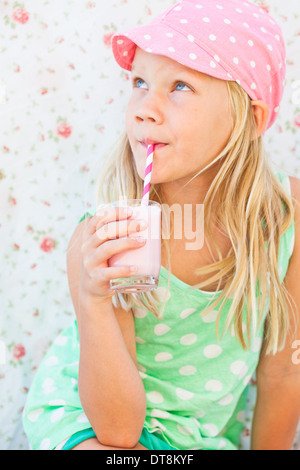 Cute young girl drinking smoothie aux fruits lait de paille à rayures sur le verre tenu en main Banque D'Images