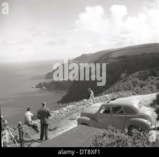 Photo historique de 1950 montrant trois hommes adultes sur le haut d'une falaise donnant sur la mer et les collines environnantes. Banque D'Images