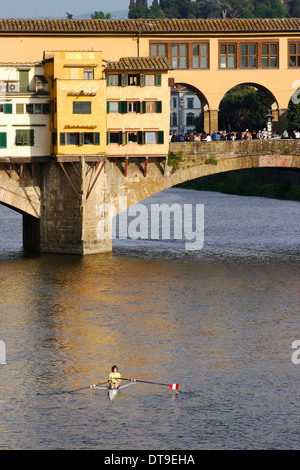 De l'aviron sur l'Arno, dans l'éclairage d'après-midi chaud, au Ponte Vecchio à Florence avec foule de touristes sur le pont Banque D'Images