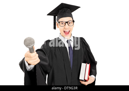 Young man in graduation gown holding d'un microphone et de livres Banque D'Images