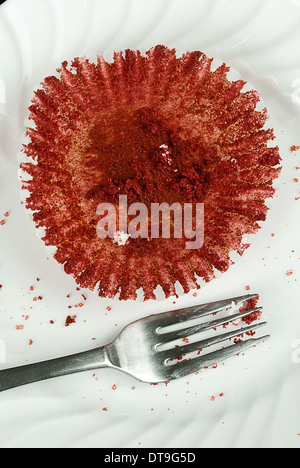 Close-up of an empty red velvet cupcake wrapper allongé sur une plaque couverte de miettes à l'aide d'une fourchette à côté. Banque D'Images