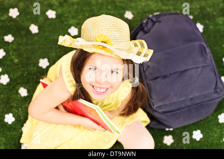 La mode cute little girl sitting on grass avec sac à dos et les portables Banque D'Images