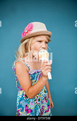 Cute young girl eating ice cream cone vanille à l'extérieur contre le mur bleu Banque D'Images