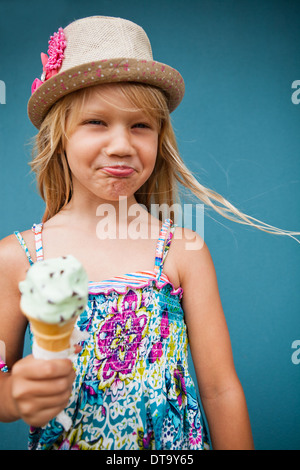 Cute young girl avec expression drole holding ice cream cone à l'extérieur contre le mur bleu Banque D'Images