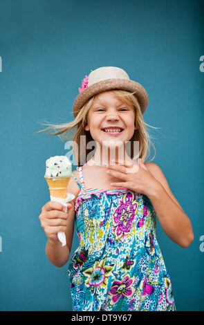 Cute smiling young girl holding ice cream cone à l'extérieur contre le mur bleu Banque D'Images