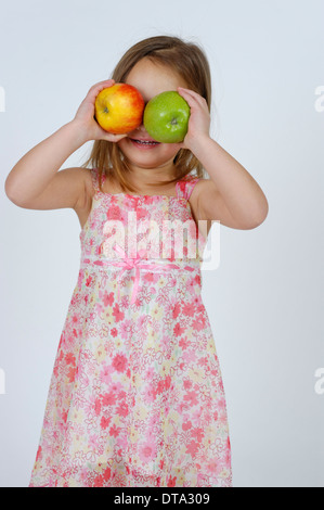 Fille avec un rouge et une pomme verte en face de son visage Banque D'Images