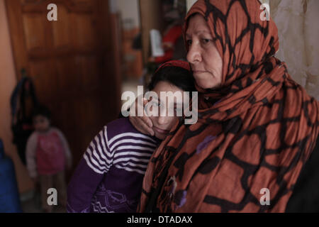 Gaza, bande de Gaza. Feb 13, 2014. Un 12-year-old fille palestinienne Rula Ali (C), qui souffre d'une laryngite chronique, est vu dans l'un de ses bras des reletives à sa maison dans le camp de réfugiés de Nuseirat, centre de la bande de Gaza, le 13 février 2014. Plusieurs patients palestiniens comme Rula qui sont en quête d'un traitement en Israël se sont vu refuser l'accès par les autorités israéliennes par Erez avec Gaza pour la tenue de documents en utilisant le terme "État de Palestine". © Wissam Nassar/Xinhua/Alamy Live News Banque D'Images