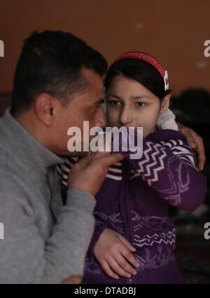 Gaza, bande de Gaza. Feb 13, 2014. Un 12-year-old fille palestinienne Rula Ali (R), qui souffre d'une laryngite chronique, est embrassé par l'un de ses proches à sa maison dans le camp de réfugiés de Nuseirat, centre de la bande de Gaza, le 13 février 2014. Plusieurs patients palestiniens comme Rula qui sont en quête d'un traitement en Israël se sont vu refuser l'accès par les autorités israéliennes par Erez avec Gaza pour la tenue de documents en utilisant le terme "État de Palestine". © Wissam Nassar/Xinhua/Alamy Live News Banque D'Images