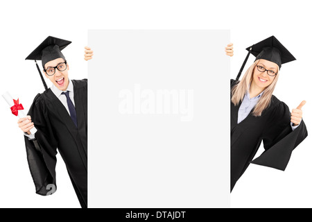 Young man in graduation gown holding diploma et une fille giving thumb up derrière panneau vierge Banque D'Images