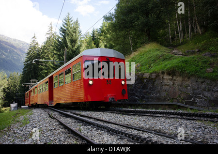 Un train rouge et blanc du train à crémaillère du Montenvers grimpe dans les arbres au-dessus de Chamonix en France. Banque D'Images