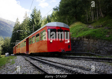 Un train rouge et blanc du train à crémaillère du Montenvers grimpe dans les arbres au-dessus de Chamonix en France. Banque D'Images