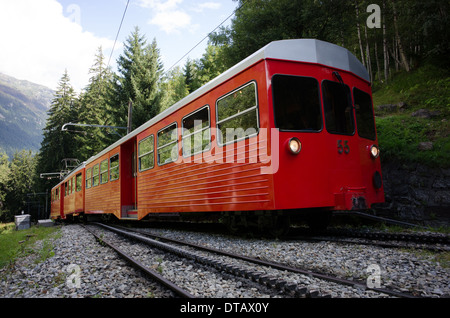 Un train rouge et blanc du train à crémaillère du Montenvers grimpe dans les arbres au-dessus de Chamonix en France. Banque D'Images