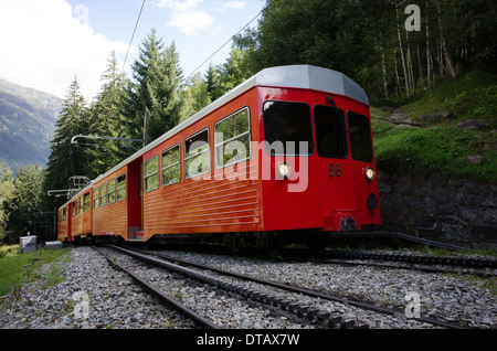 Un train rouge et blanc du train à crémaillère du Montenvers grimpe dans les arbres au-dessus de Chamonix en France. Banque D'Images