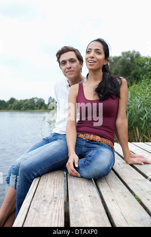 Young couple sitting on wooden pier, smiling Banque D'Images
