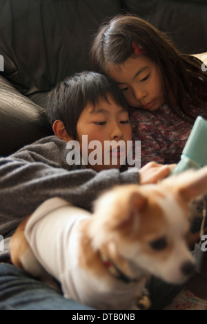 Un frère et une soeur lying on sofa with dog Banque D'Images