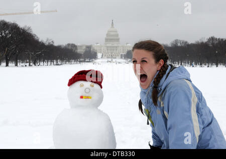 Washington DC, USA. Feb 13, 2014. Une femme de poser pour des photos avec un bonhomme en face du Capitole sur le National Mall à Washington DC, capitale des États-Unis, le 13 février 2014. La tempête de l'hiver aux États-Unis d'états du sud a apporté beaucoup de neige et de grésil de congélation pour le nord-est le jeudi, la fermeture des agences fédérales, les écoles et les aéroports tout en laissant un demi-million de personnes sans électricité. La neige et la glace a rendent les déplacements difficiles pour les navetteurs dans le centre-ville de D.C. zone comme le gouvernement local a exhorté les résidents à rester à l'intérieur et de la routes dangereuses. Banque D'Images