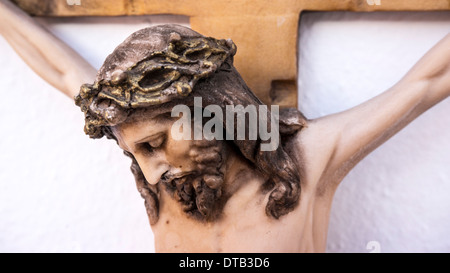 Vue détaillée tête avec couronne d'épines qui touchent à peu de plâtre peint la souffrance Jésus sur les montées sur mur de plâtre blanc Banque D'Images