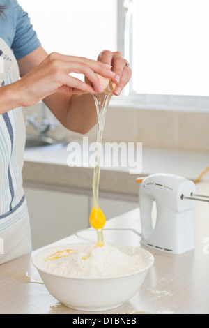 Mid section of woman cracking un oeuf dans un bol de cuisine Banque D'Images