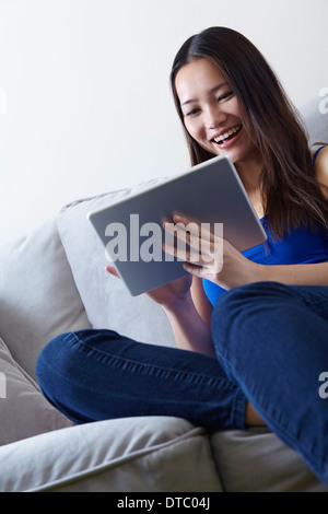 Young woman sitting on sofa using digital tablet Banque D'Images