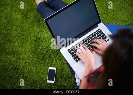 Jeune femme assise sur un tapis à l'aide d'ordinateur portable Banque D'Images