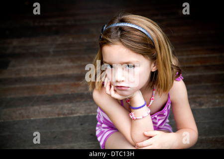 Sullen young girl sitting on porch with hands on chin Banque D'Images